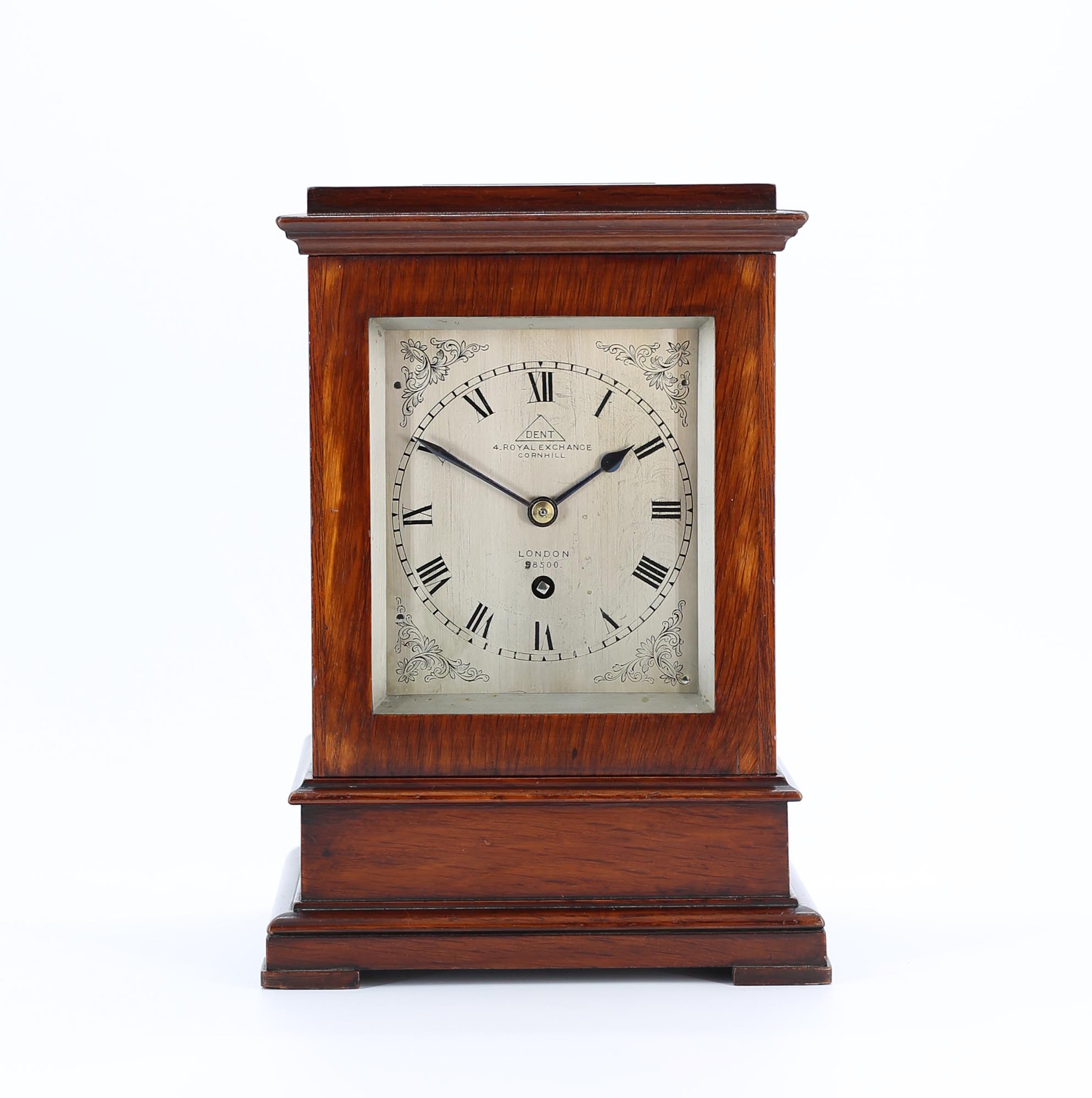 Fusee Five Glass Library Clock by Dent A quality 8-day timepiece movement, with chain fusee, an anchor escapement and a London-style pendulum. The back plate is engraved ‘Dent, 4 Royal Exchange, Cornhill’ and also features a pendulum lock for use when transporting the clock. Silvered brass dial similarly signed Dent, 4 Royal Exchange, with engraved Roman numerals and floral swags to the corners, all within a silvered mask. Original non-matching blued steel hands. The case of dark satinwood features glass to the front, back, sides and top, and locking doors. Please note that this clock has been photographed before restoration. C.1870 Height: 9 ¾” 25cm £ 4,950